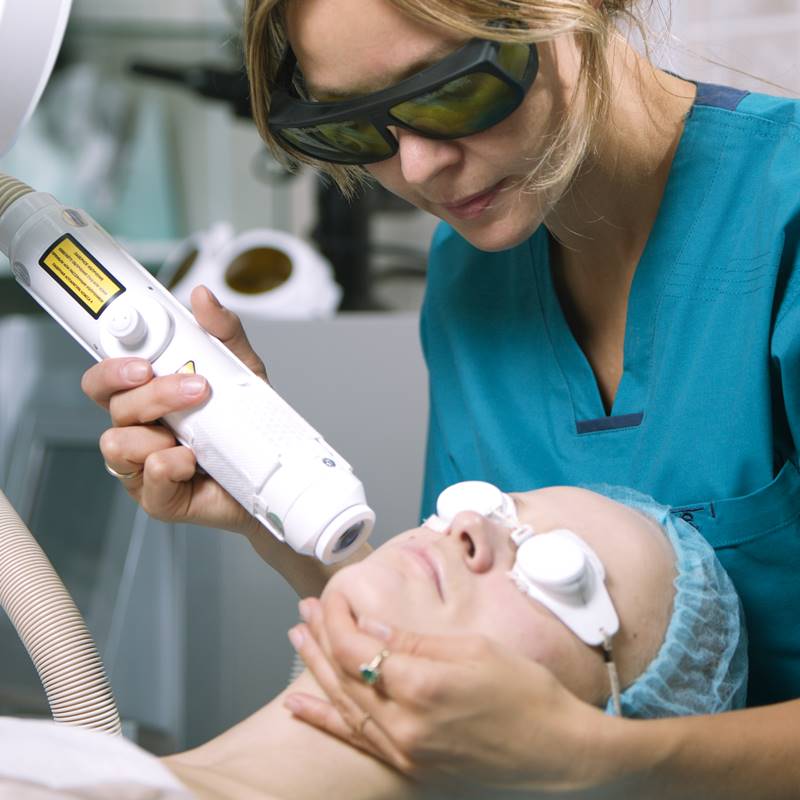 A woman undergoing a laser facial treatment at a clinic.