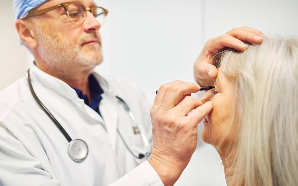 Doctor examining an elderly woman's eye with a penlight.