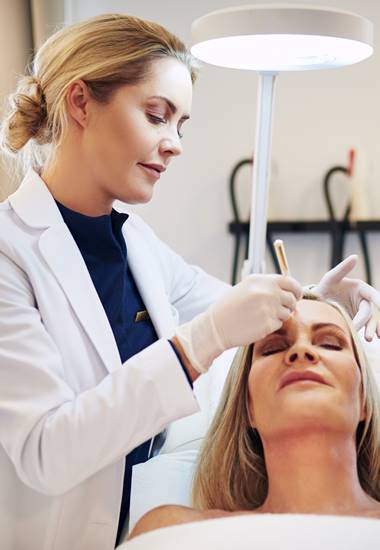 A professional applies cosmetic treatment to a woman's forehead.