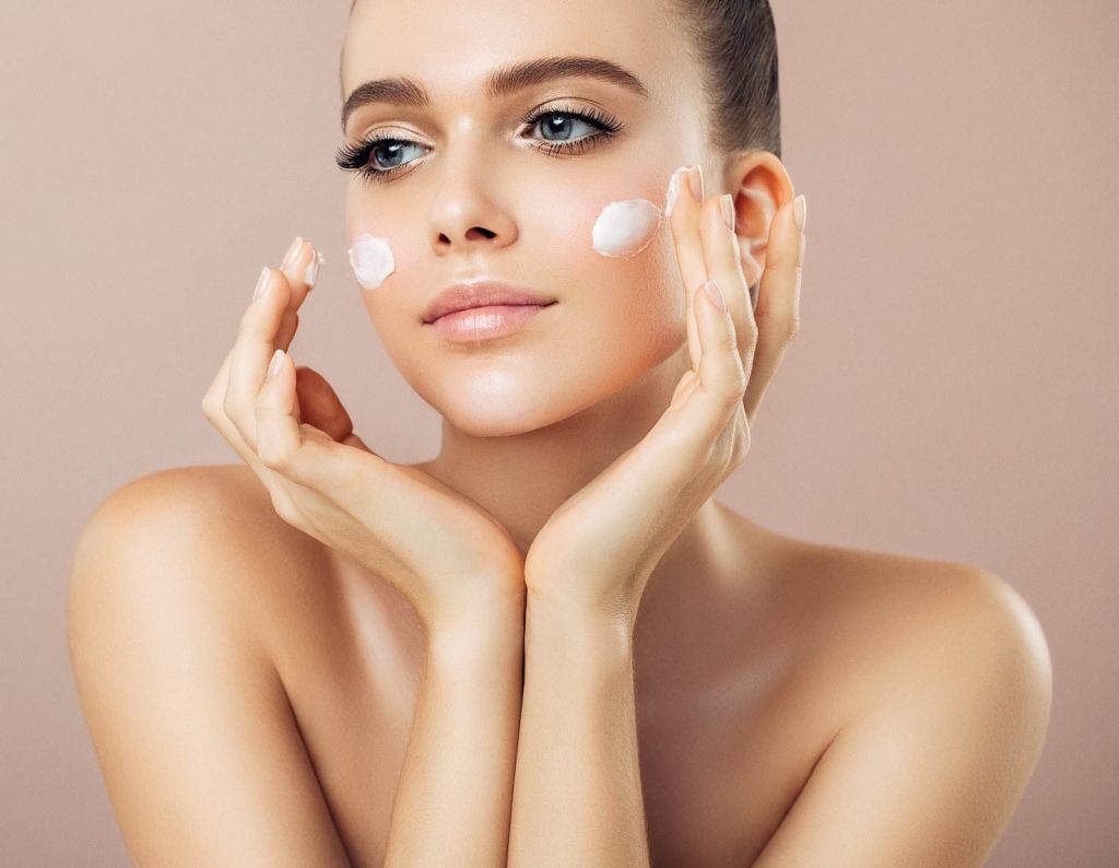 Woman applying moisturizer on her face with a serene expression.
