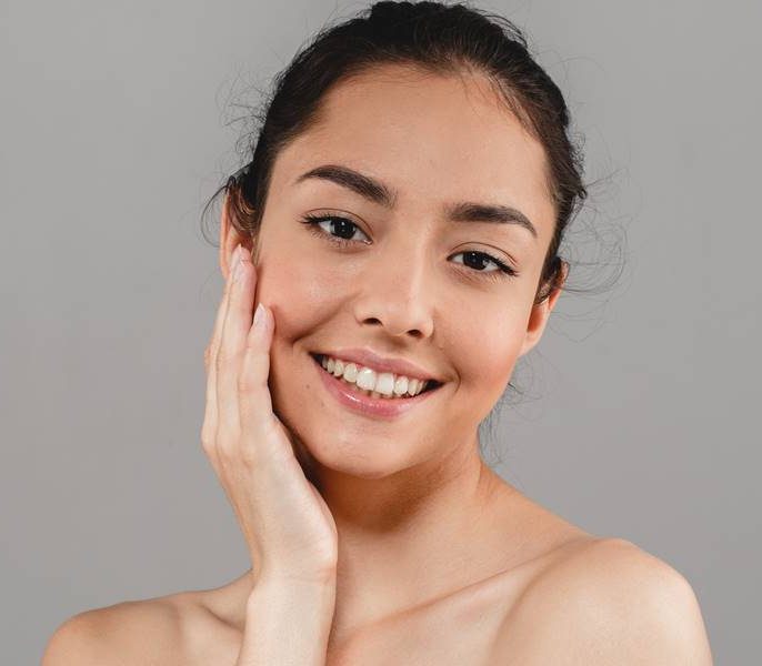 Smiling woman with clear skin gently touching her face.