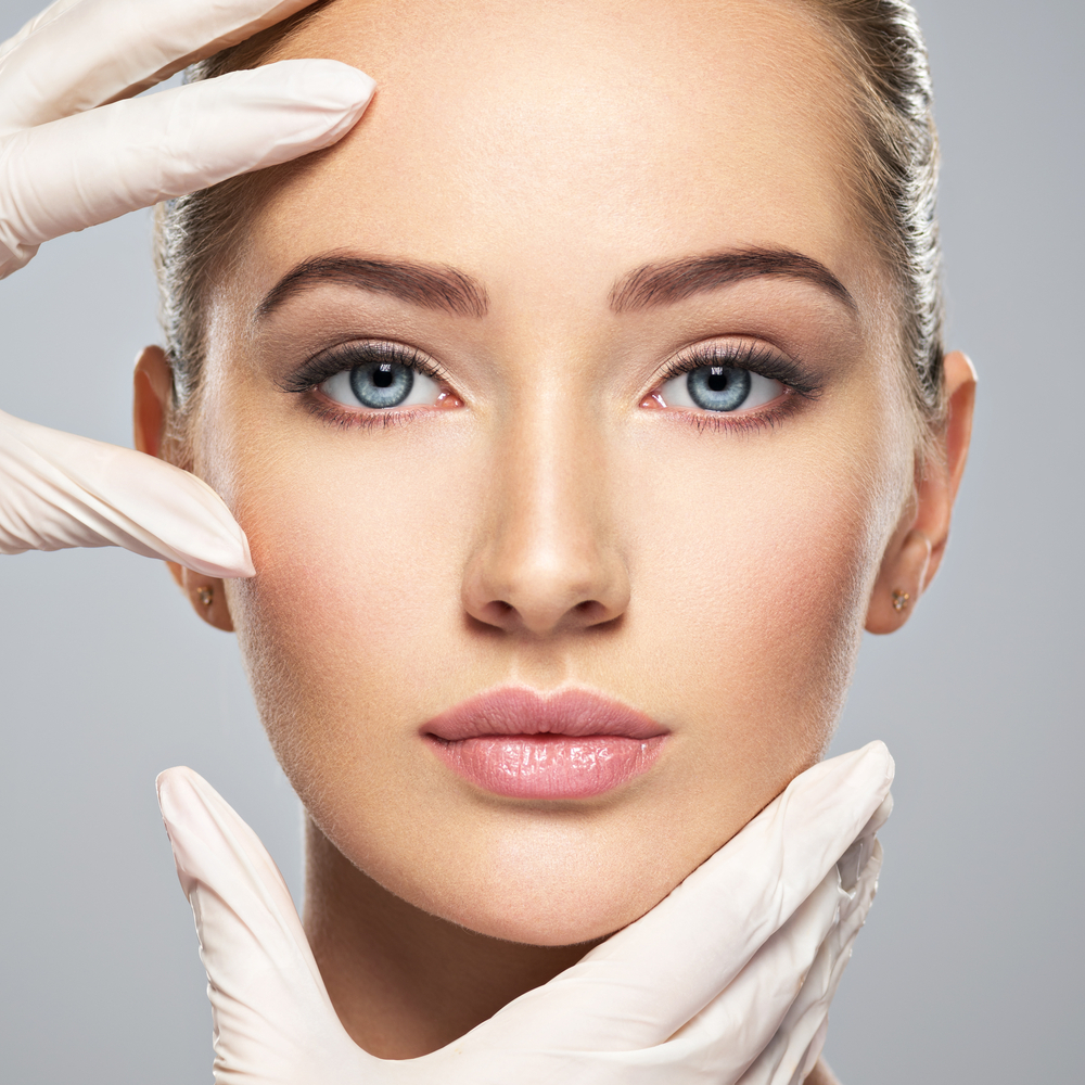 Close-up of a woman's flawless face framed by gloved hands in a skincare setting.