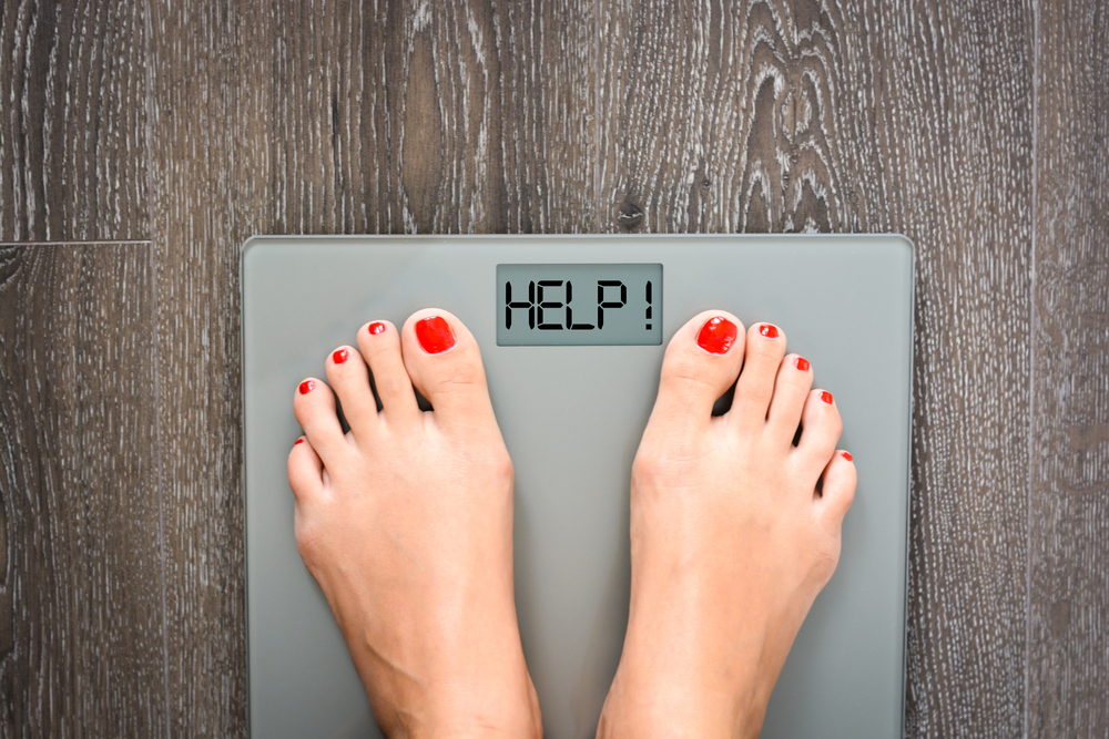Feet with red nail polish on a scale showing 'HELP!' instead of numbers.