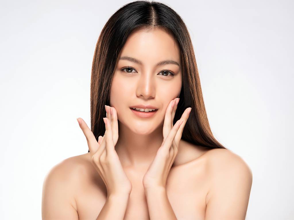 A woman with clear skin gently touching her face, smiling softly.