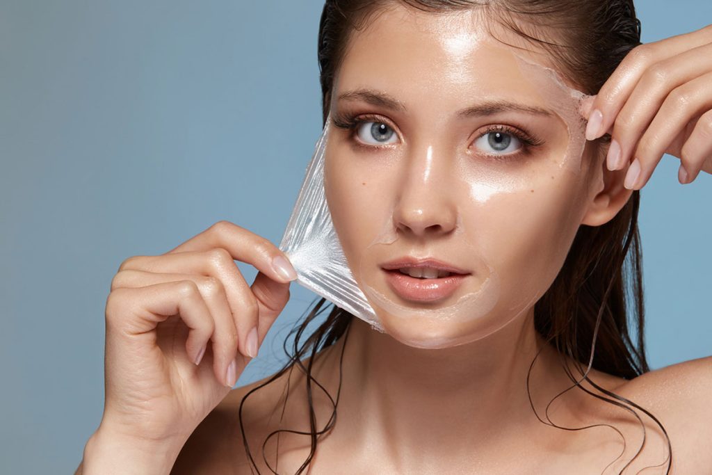 Woman peeling off a clear facial mask, revealing glowing skin.