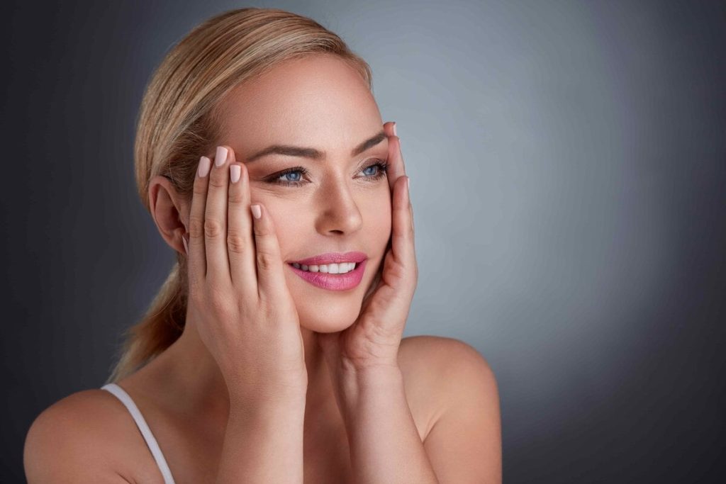Smiling woman gently touching her face with a serene expression.
