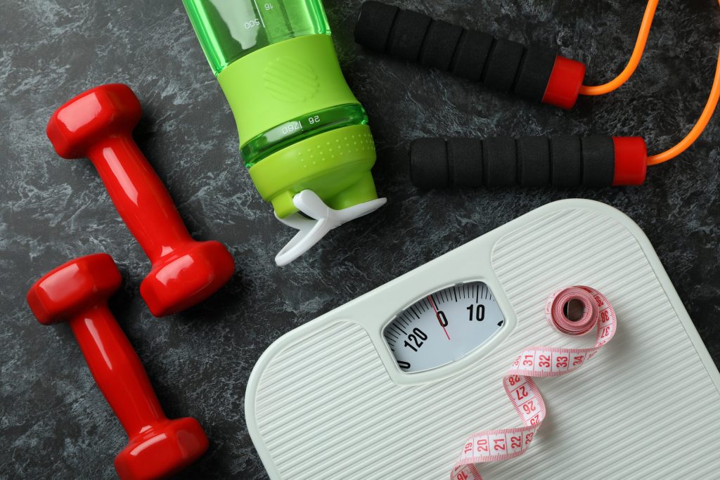 Fitness equipment and a scale on a dark surface with a measuring tape.