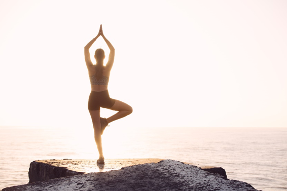 Person practicing yoga on a rock at sunrise by the sea.