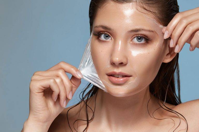 Woman peeling off a transparent facial mask, showing glowing skin.